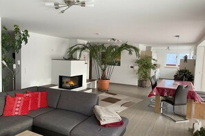 Una sala de estar moderna con chimenea, un comedor con mesa y sillas, y varias plantas en macetas.