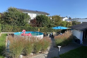 Een achtertuin van een woning met een zwembad, een flamingo-opblaasbad en een terras met een tafel en stoelen.