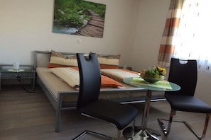Un dormitorio con una cama, dos sillas, una mesa con un frutero y un cuadro en la pared.