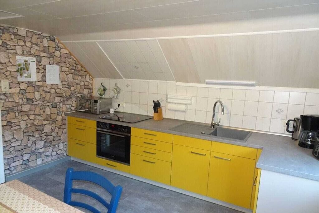 A kitchen with yellow cabinets, a stone wall, and a blue chair.