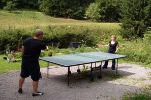A ping pong table set up outdoors with a gravel surface, surrounded by greenery. - Holiday apartment in Suhl with swimming pool (Suhl)