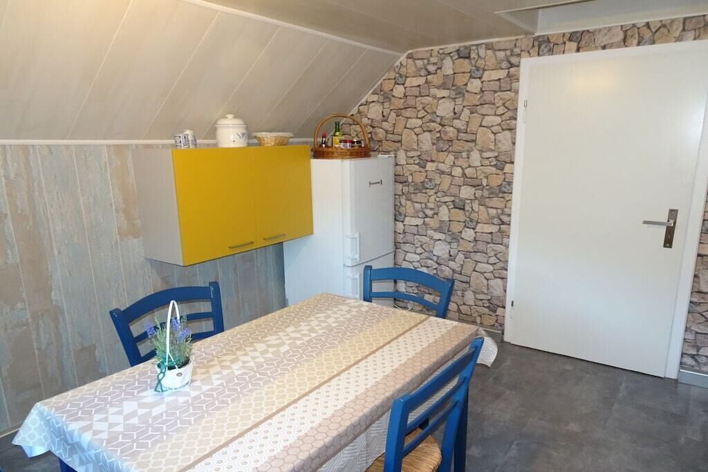Uma sala de jantar com uma mesa posta para dois, um armário amarelo acima e uma parede de pedra à direita.