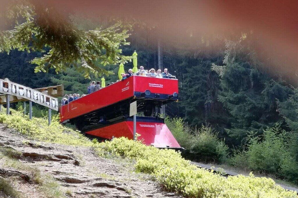 Un autobús rojo de dos pisos en una carretera, con un puente al fondo.