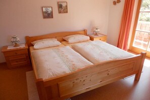 En træseng med to puder, et natbord med en lampe og et vindue med gardiner.