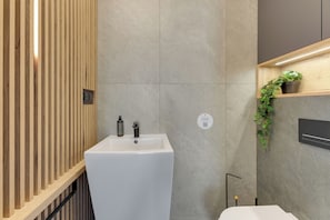 A modern bathroom with a wooden panel wall, a white sink, a black faucet, a potted plant, and a wall-mounted light fixture. - Nowa Letnica - Gdańsk Panoramic View  (Gdańsk)