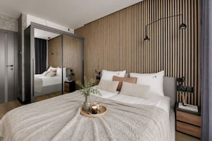 A modern bedroom with a large bed, a mirror, and a wooden slat wall. - Nowa Letnica - Gdańsk Panoramic View  (Gdańsk)