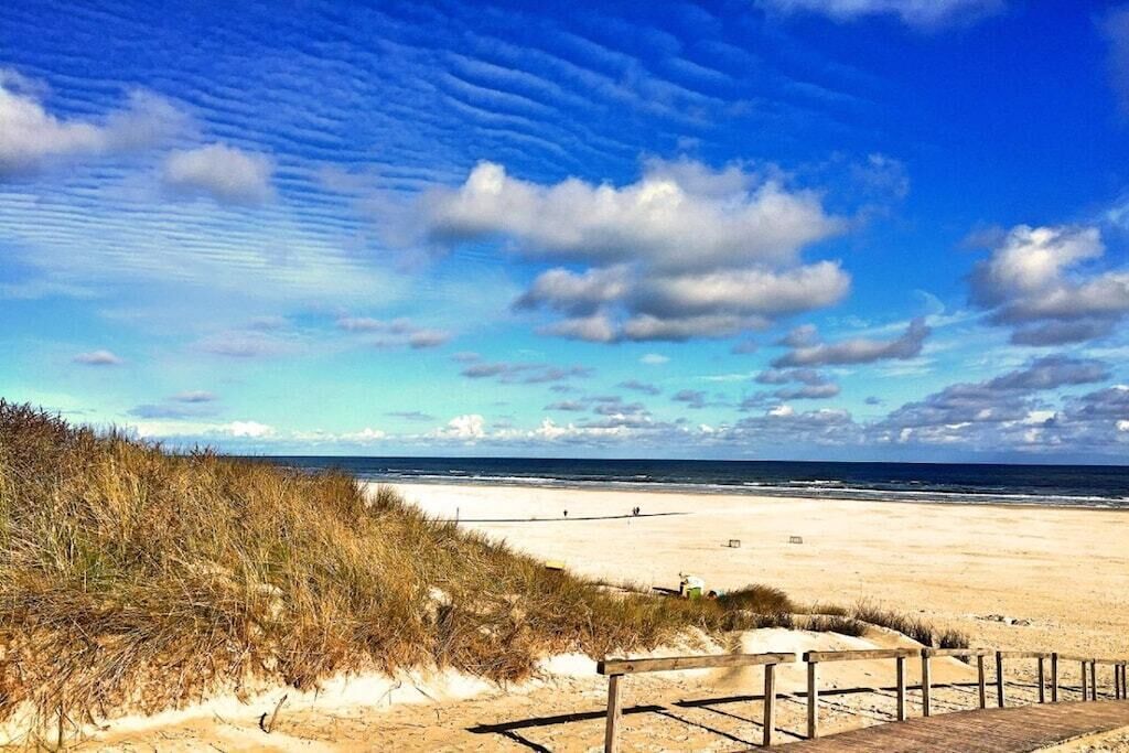 A beach with a wooden walkway leading to the shore, sandy dunes, and the ocean.