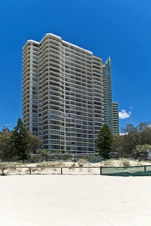 A high-rise building with multiple balconies, located near a sandy area with sparse vegetation. - Beachfront| Ocean Views|Pool & Spa|Sleeps 5|Tennis Court| 2 Bedroom 2 Bathroom (Surfers Paradise)