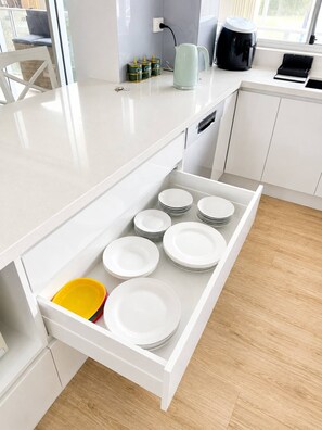 A kitchen with a white countertop, a drawer with stacked plates, and a coffee maker on the counter. - Beachfront| Ocean Views|Pool & Spa|Sleeps 5|Tennis Court| 2 Bedroom 2 Bathroom (Surfers Paradise)