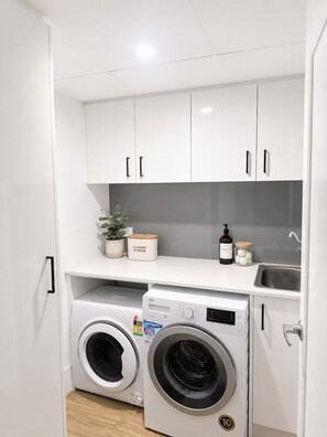 A compact laundry area with two front-loading washing machines, a sink, and storage cabinets. - Beachfront| Ocean Views|Pool & Spa|Sleeps 5|Tennis Court| 2 Bedroom 2 Bathroom (Surfers Paradise)