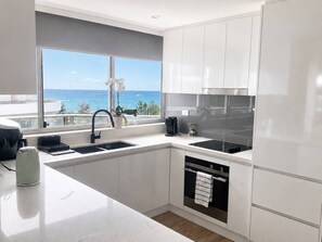 A modern kitchen with white cabinets, a black sink, and an oven. There is a window with a view of the ocean. - Beachfront| Ocean Views|Pool & Spa|Sleeps 5|Tennis Court| 2 Bedroom 2 Bathroom (Surfers Paradise)