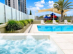 A swimming pool with a water feature, surrounded by lounge chairs and a playground in the background. - Beachfront| Ocean Views|Pool & Spa|Sleeps 5|Tennis Court| 2 Bedroom 2 Bathroom (Surfers Paradise)
