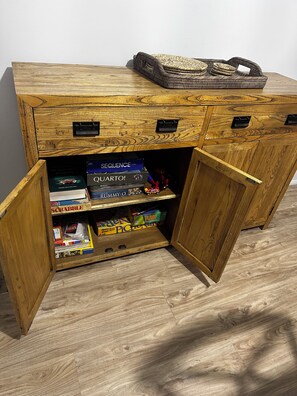 A wooden cabinet with open doors revealing board games and a basket on top. - Beachfront| Ocean Views|Pool & Spa|Sleeps 5|Tennis Court| 2 Bedroom 2 Bathroom (Surfers Paradise)