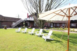 Ein grünes, offenes Gelände mit weißen Stühlen und einem großen Sonnenschirm.