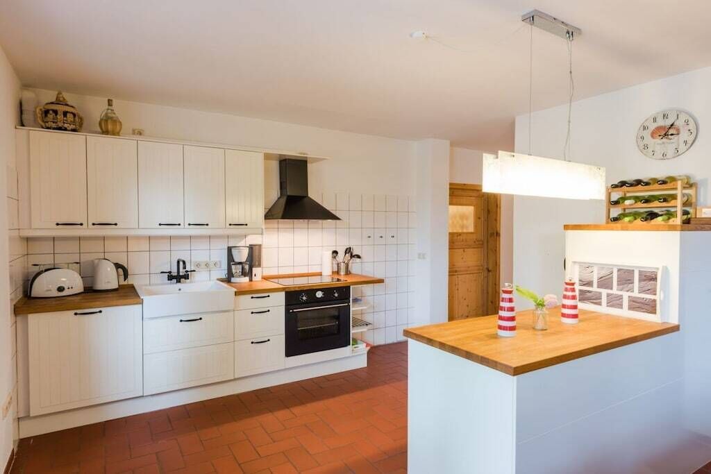 Una cocina con armarios blancos, encimera de madera, estufa y lámpara colgante.