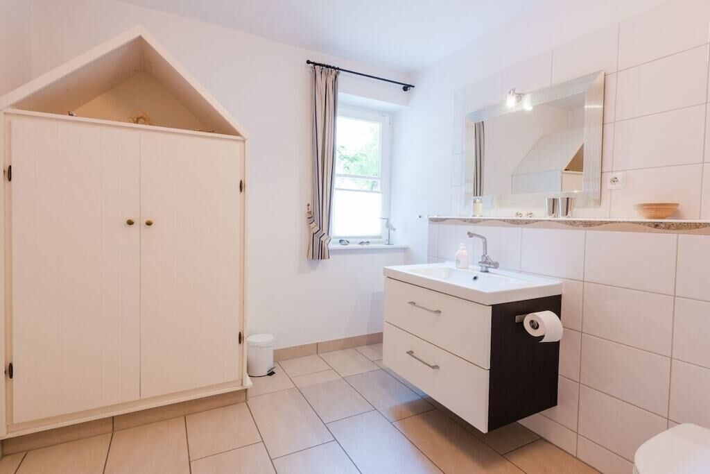 Ein Badezimmer mit weißem Waschtisch, einem Spiegel, einer Toilette und einem Fenster mit Vorhängen.