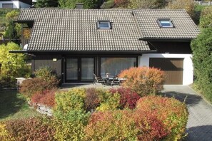 A house with a tiled roof, a garage, and a garden with various shrubs.