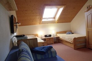 A small, cozy room with a sloped ceiling, a skylight, a bed, a sofa, and a desk with a computer.