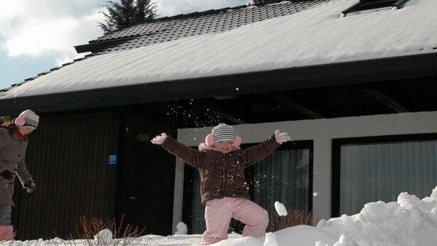 Een kind speelt in de sneeuw, met een gebouw op de achtergrond.