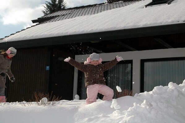 A child playing in the snow with a building in the background.