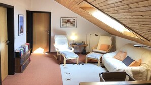 Een gezellige kamer met een schuine kap, een bank, twee fauteuils, een klein tafeltje en een boekenkast.