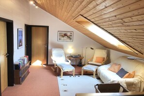 A cozy room with a sloped ceiling, a sofa, two armchairs, a small table, and a bookshelf.