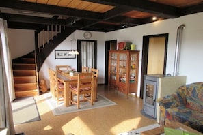 A cozy living room with a wooden staircase, a dining table with chairs, a cabinet with glass doors, and a sofa.