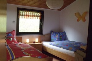 Habitación con dos camas, una ventana con cortinas, una mesita de noche con lámpara y un adorno en la pared.