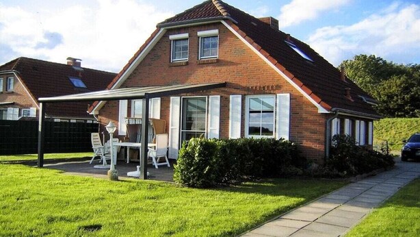 A two-story house with a covered patio area, a lawn, and a car parked in the driveway. - Holiday home with 3 bedrooms (Neßmersiel)