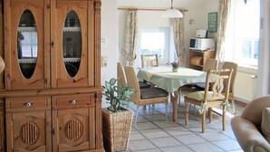 A dining area with a table, chairs, a cabinet, and a hanging light fixture. - Holiday home with 3 bedrooms (Neßmersiel)