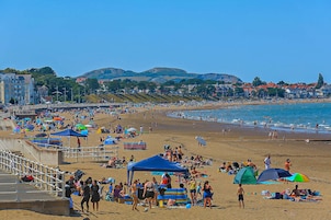 Una playa concurrida, gente, tiendas de campaña y sombrillas.