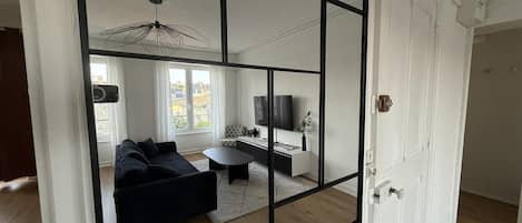 Un salon moderne avec un canapé d’angle, une table basse, un téléviseur et un luminaire suspendu.