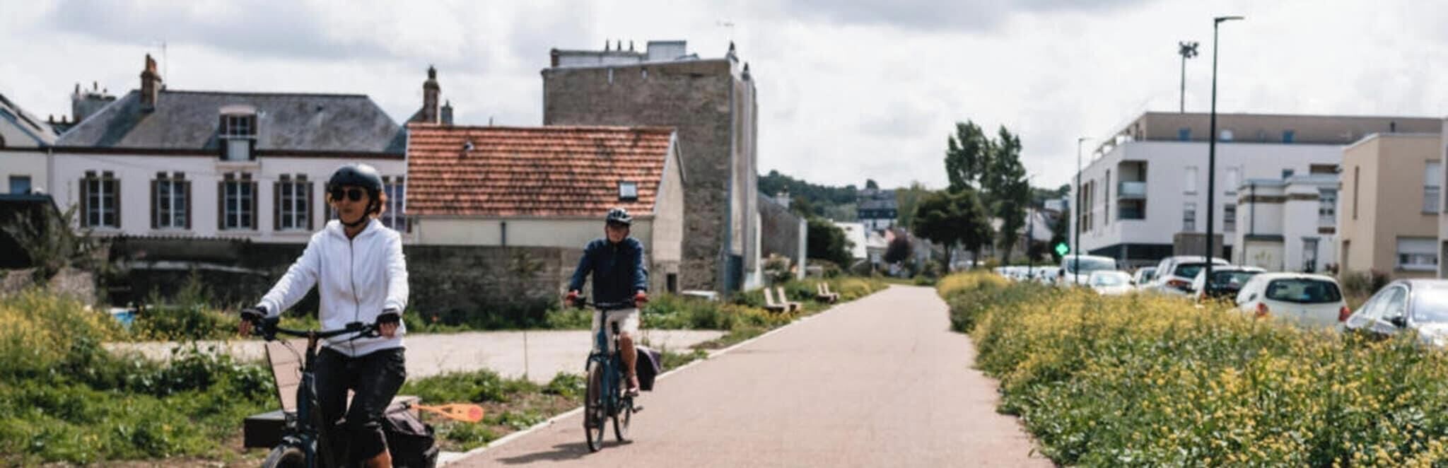 Ein gepflasterter Weg mit Radfahrern, umgeben von Grünflächen und Gebäuden.