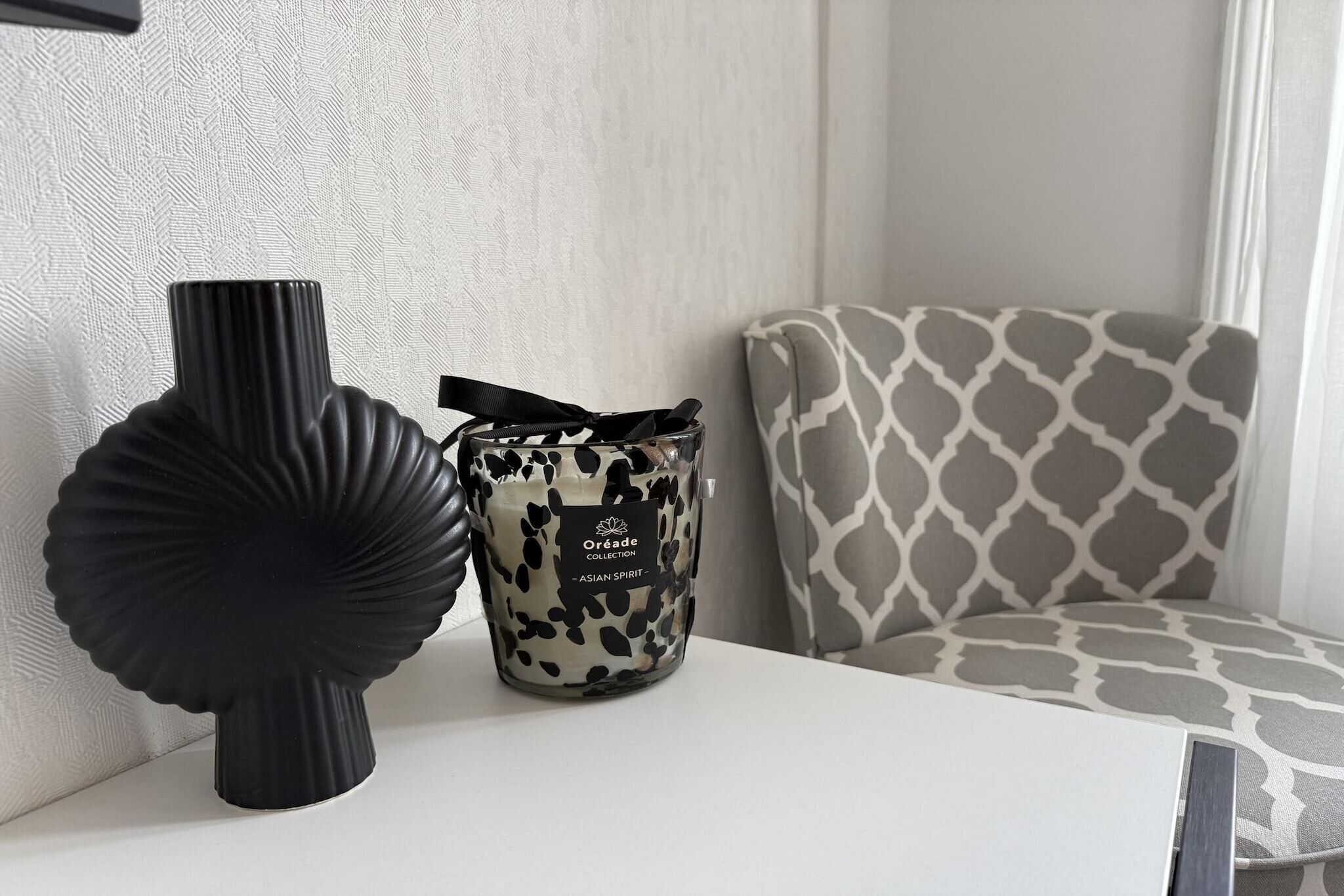 Une table blanche avec un vase noir et un chandelier à motifs.