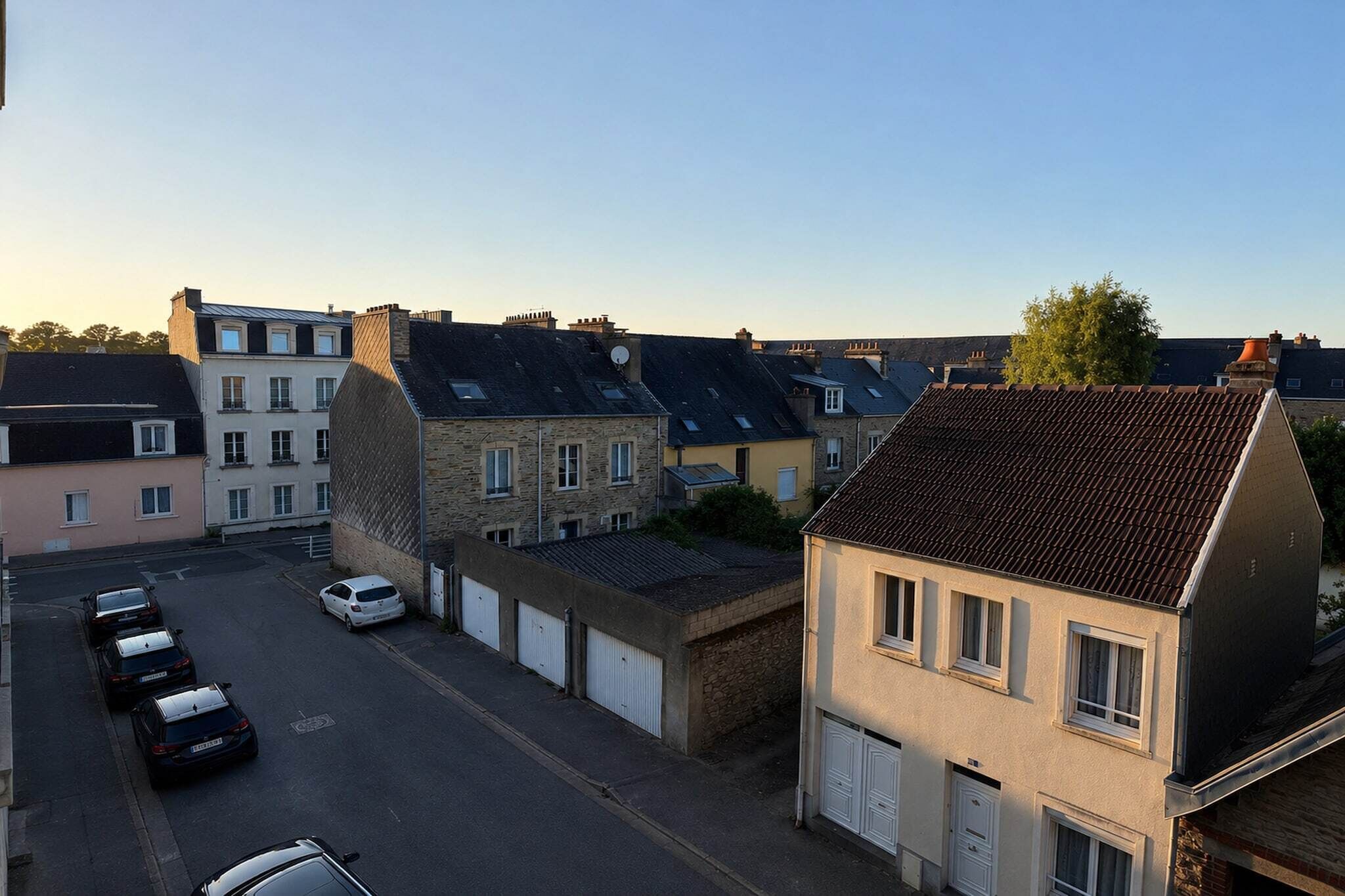 Eine Wohnstraße mit geparkten Autos und Häusern mit unterschiedlichen Dachformen und -farben.