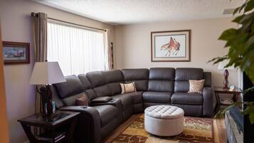 Ein Eckwohnzimmer mit einem Ecksofa, einem Glastisch, einem Beistelltisch und einem Teppich.