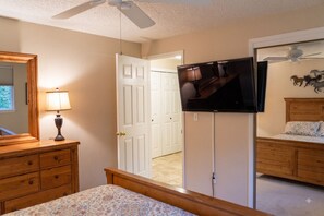 A bedroom with a bed, dresser, TV, and a door leading to another room.