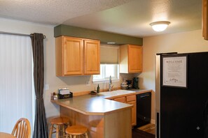A kitchen with wooden cabinets, a refrigerator, a coffee maker, and a welcome sign.