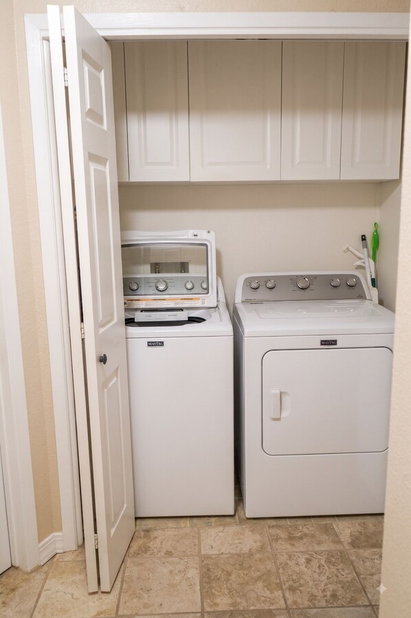 A laundry room with a front-loading washer and dryer, a white door, and a tiled floor.