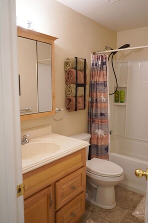 Een badkamer met een wit wastafel, houten wastafelmeubel, toilet en een douchegordijn met dierenprint.