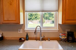 A kitchen with a white sink, a stainless steel faucet, wooden cabinets, a window with blinds, and a coffee maker on the counter.