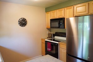 A kitchen with wooden cabinets, a stainless steel refrigerator, a microwave, an oven, and a wall clock.