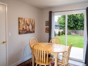 Een eethoek met een tafel en stoelen, een schilderij aan de muur en uitzicht op een achtertuin door een schuifpui.