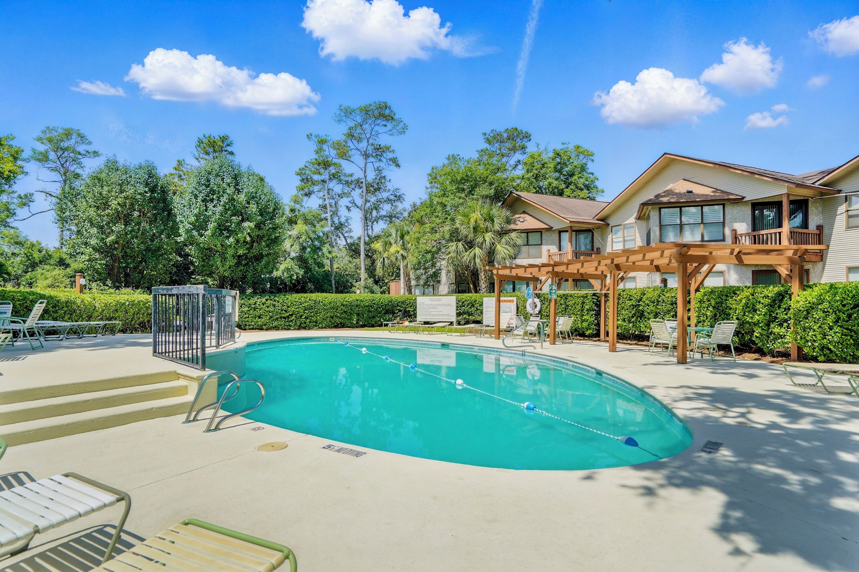 A swimming pool with a wooden deck, lounge chairs, and a house with a balcony in the background.