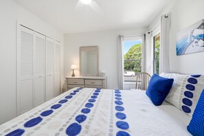 A bedroom with a bed, a dresser, a mirror, and a window with a view of the outside. - 3BR Harbour Oaks • Walk to Pier Village & Beach • Pool (St Simons)