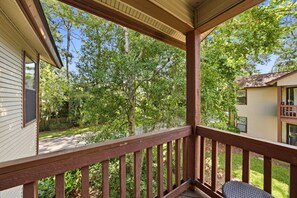 A covered porch with a wooden railing, overlooking a backyard with trees and a house. - 3BR Harbour Oaks • Walk to Pier Village & Beach • Pool (St Simons)