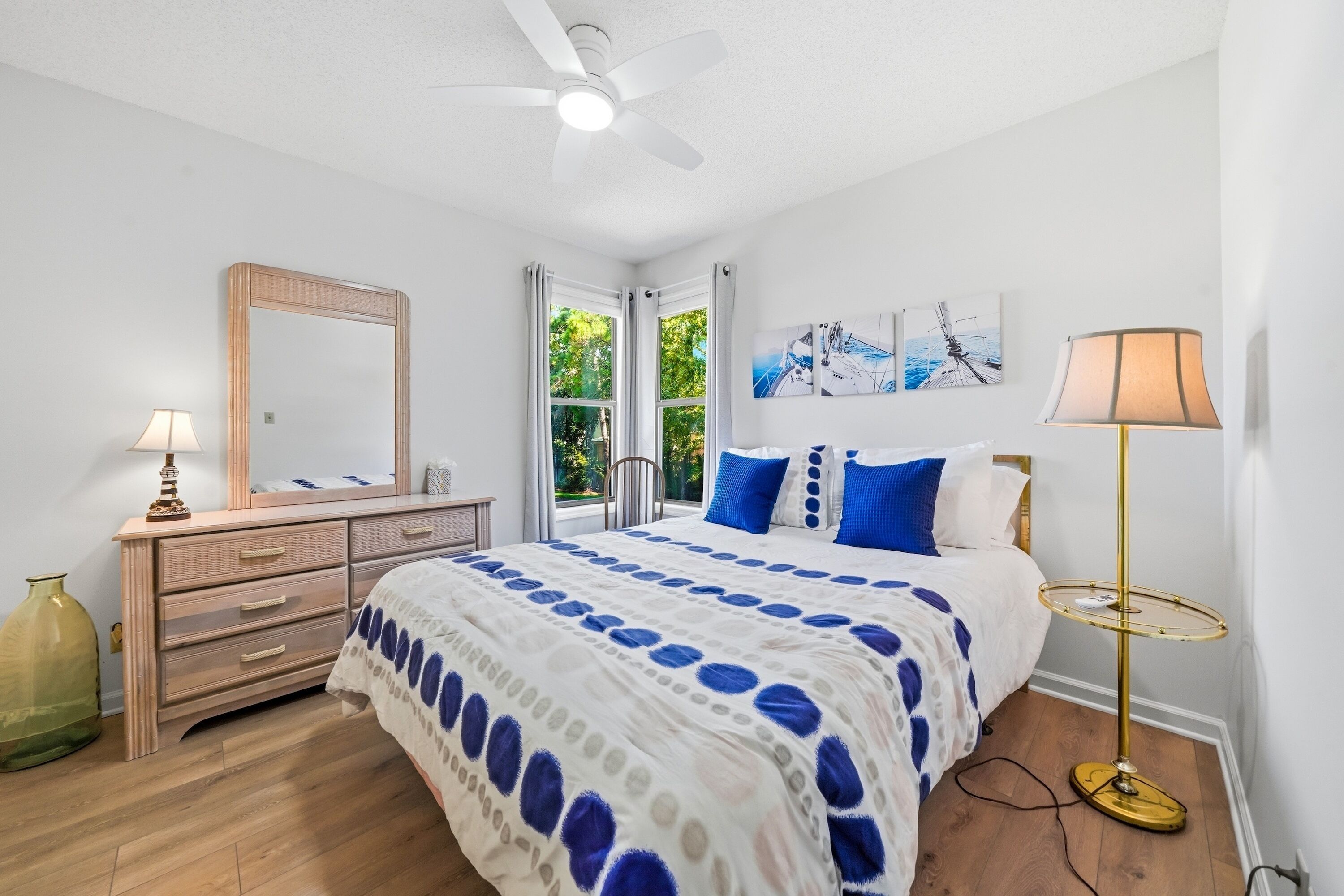 A bedroom with a bed, dresser, mirror, ceiling fan, and artwork on the wall.