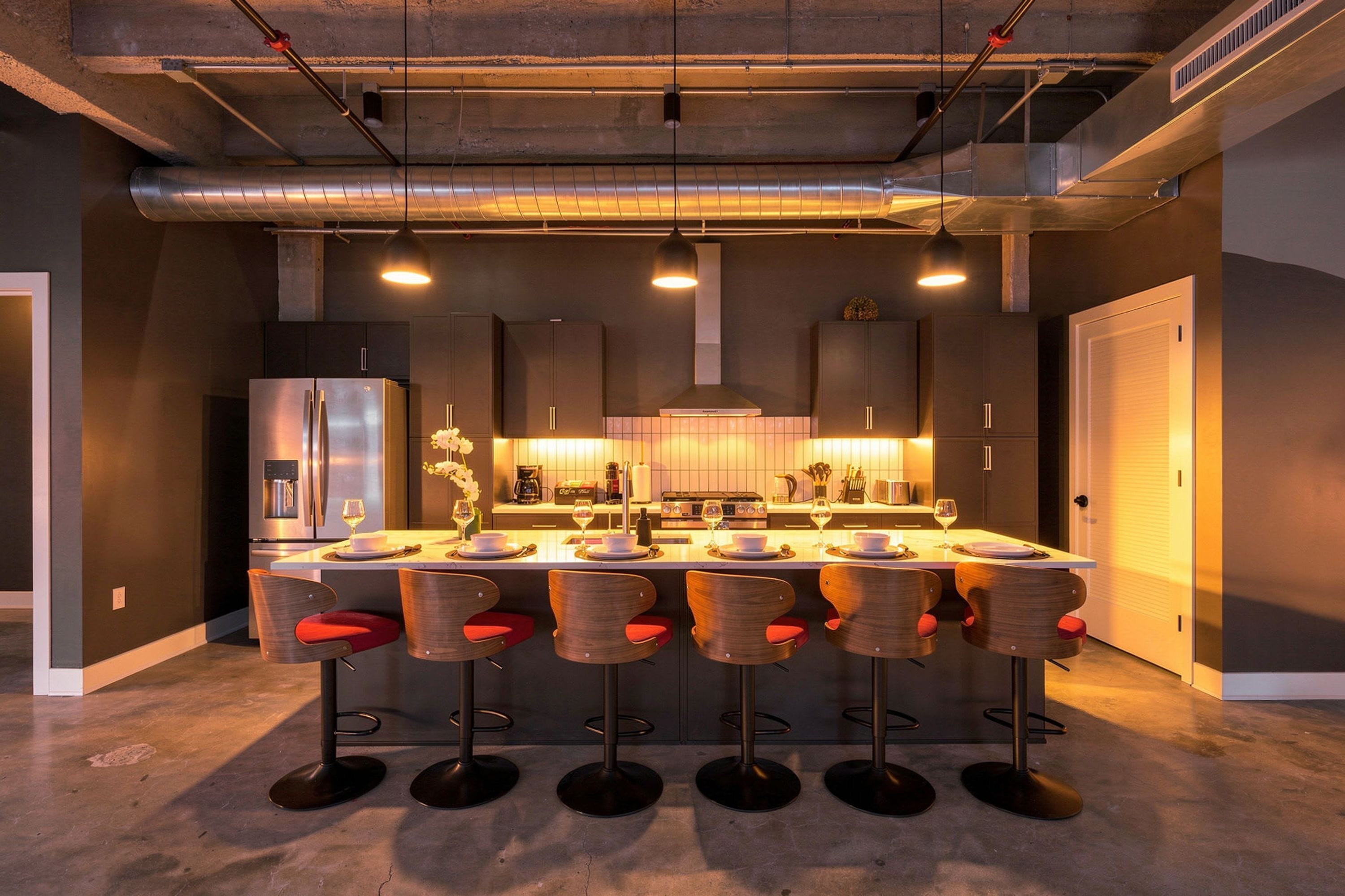 Een moderne keuken met een centraal eiland, barkrukken en roestvrijstalen apparatuur.