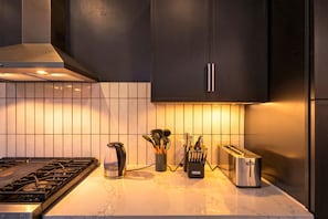 A modern kitchen with dark cabinetry, a gas stove, a kettle, a toaster, and a utensil holder. - 4BR 3BA KC Loft Collection Rooftop Bar Spa (Kansas City)