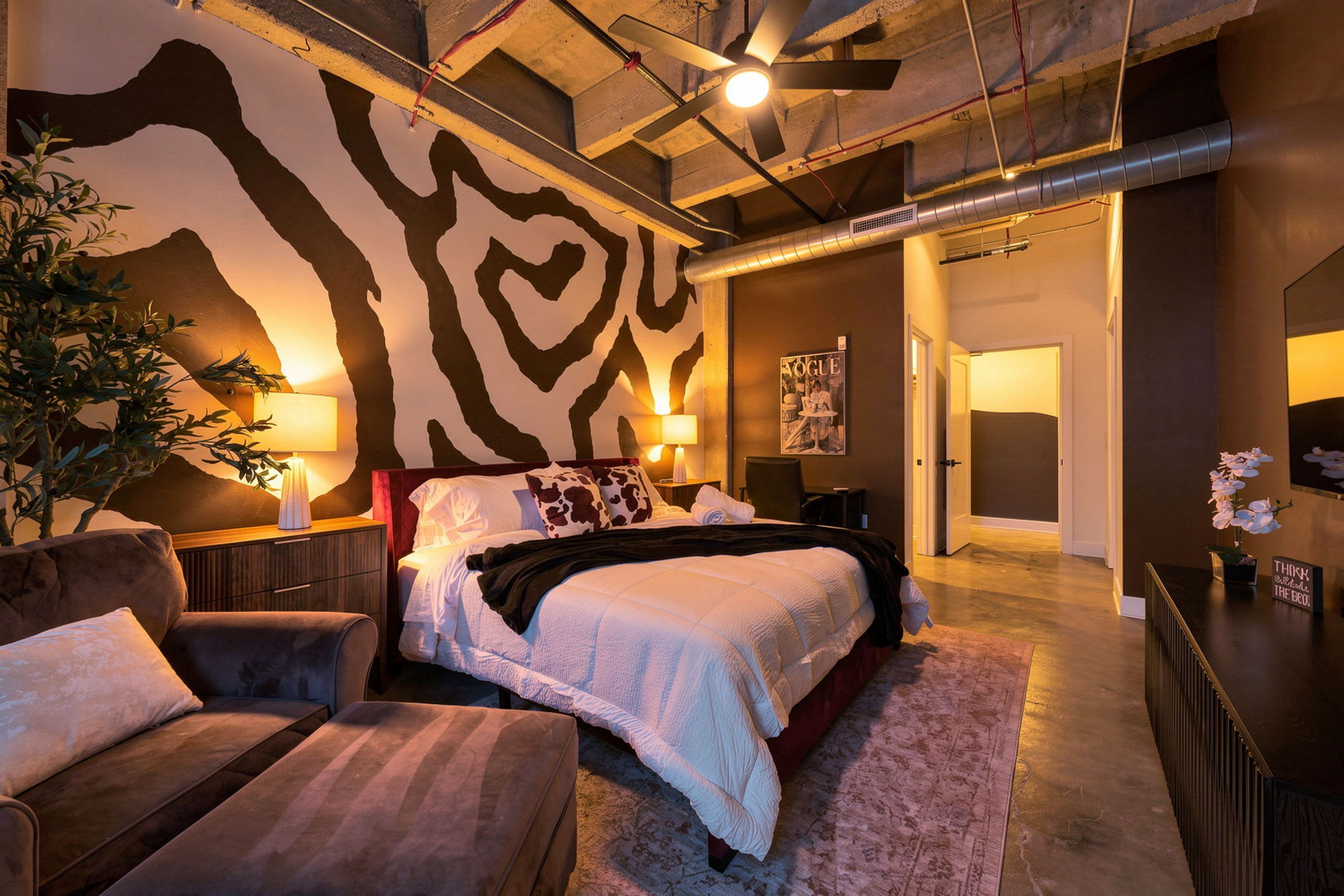 Un dormitorio moderno con pared estampada de cebra, una cama con ropa de cama blanca, un escritorio y una silla.